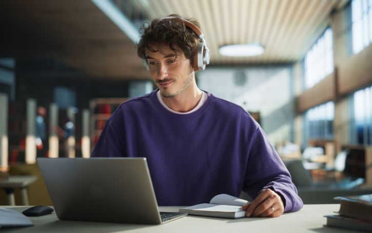 A man wears headphones while looking at his laptop